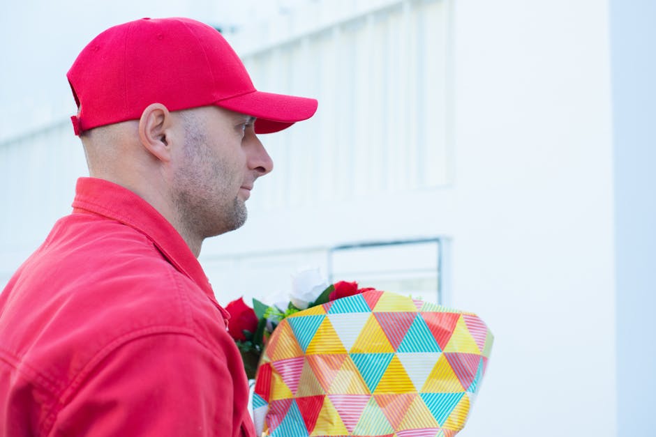 A delivery person is shown in profile, wearing a red cap and matching red jacket, holding a vibrant floral gift wrapped in geometric patterned paper featuring yellow, blue, red, and green triangles. T
